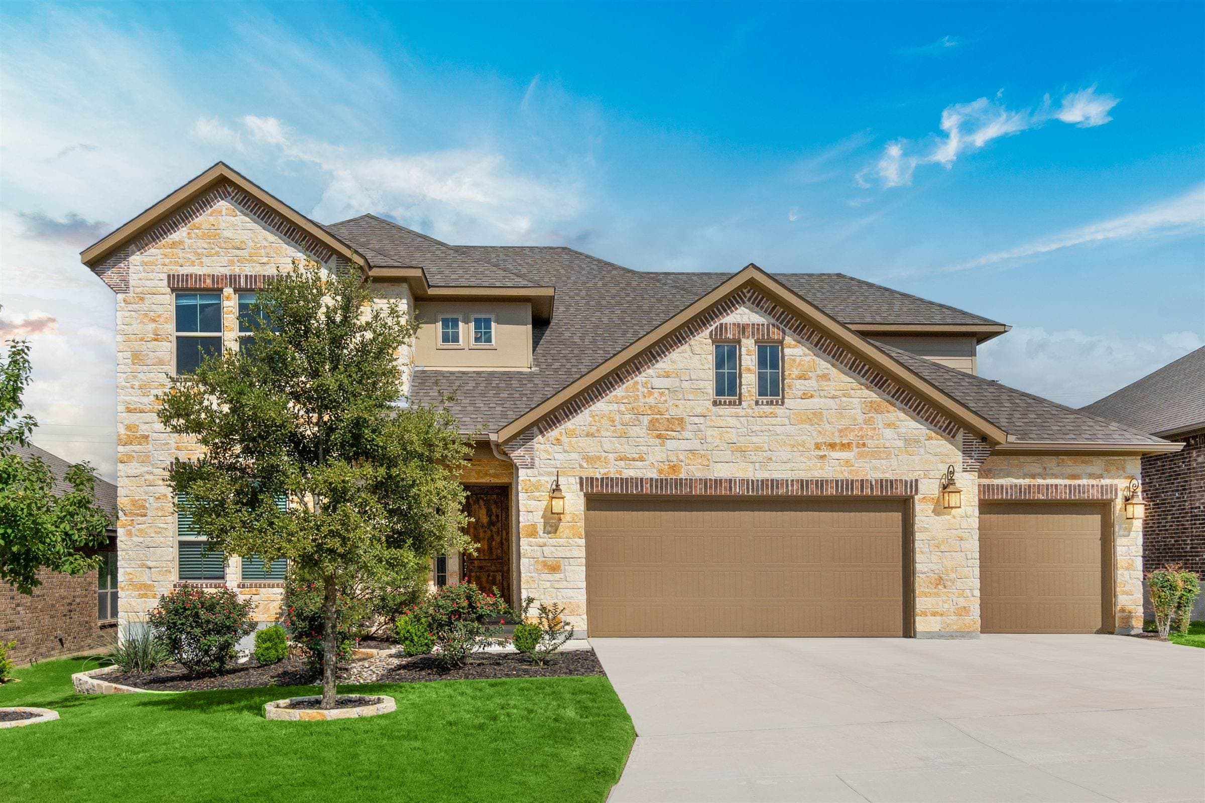 Two-story stone and siding home with large windows under a bright blue sky