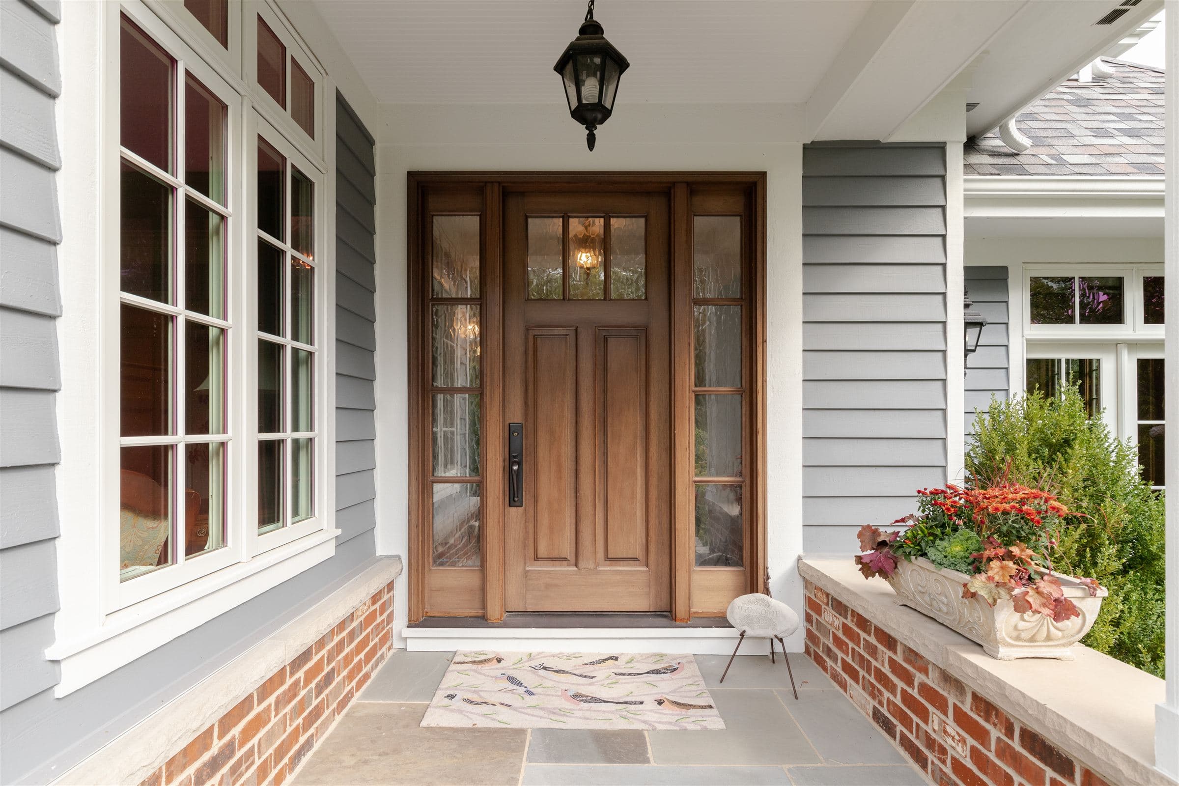 Wood front entry door with glass sidelites on a brick and siding porch