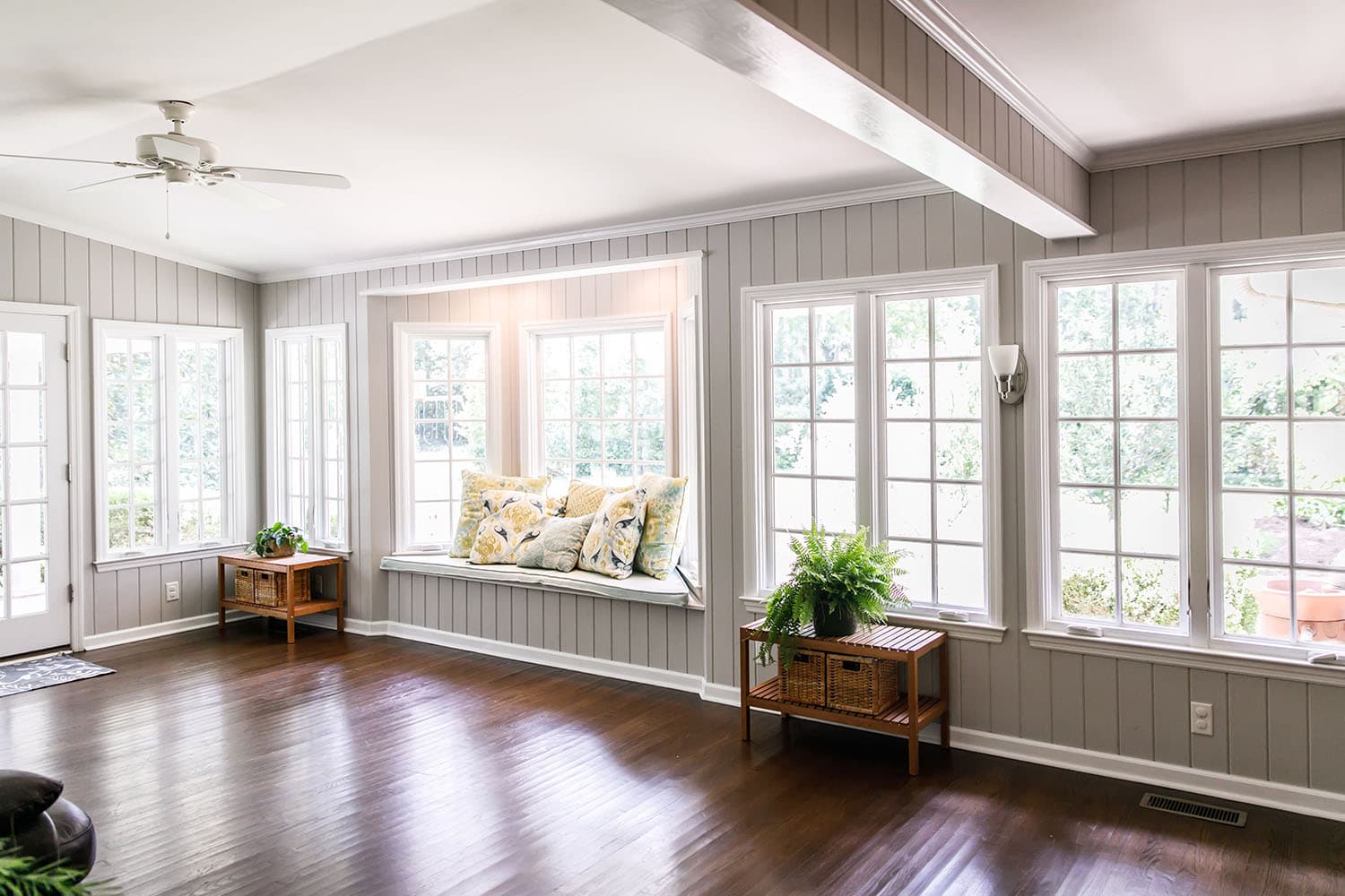 Bright sunroom lined with white-framed windows and a cushioned window seat